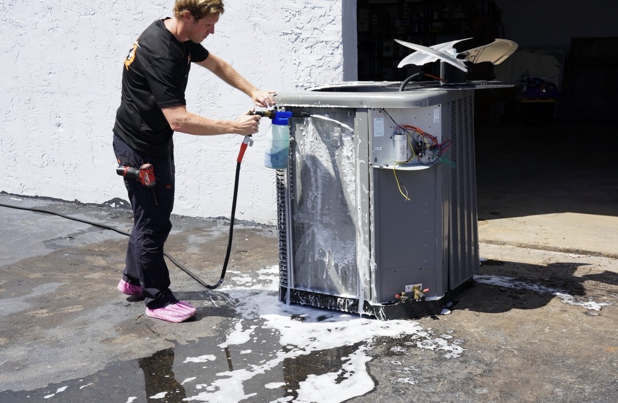 AQ AC & Electric technician foam-cleaning an AC condenser coil