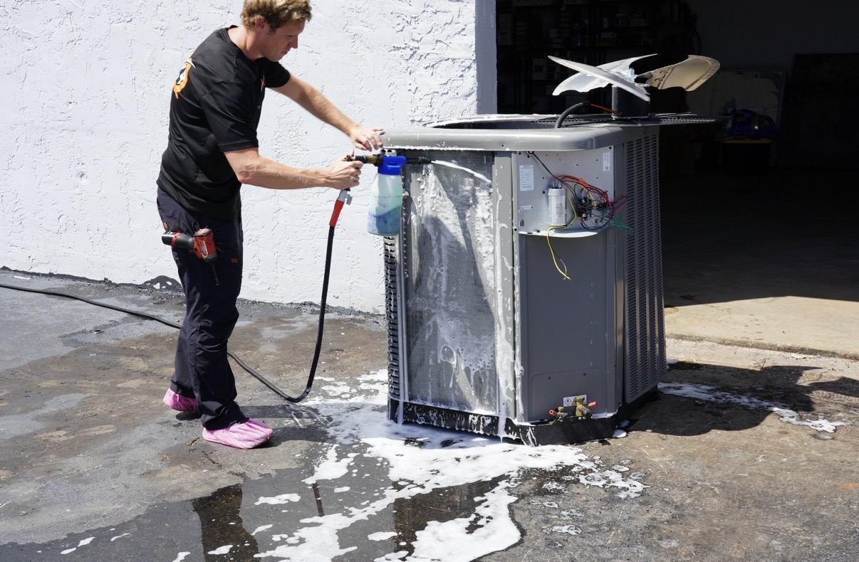 AQ AC & Electric technician foam-cleaning an outdoor AC condenser coil during an AC SuperClean maintenance and tune-up